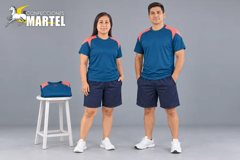 Dos modelos adultos con camisetas azul petróleo de hombros coral y shorts marinos junto a una muestra doblada.