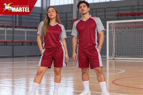 Mujer y hombre con camisetas y shorts rojo vino con paneles gris claro en cancha cubierta.