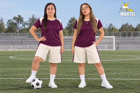 Dos mujeres adultas con camisetas ciruela y shorts marfil en una cancha de fútbol.
