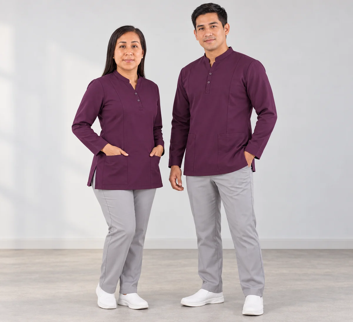 Mujer y hombre con túnicas ciruela de manga larga y pantalones grises en estudio.