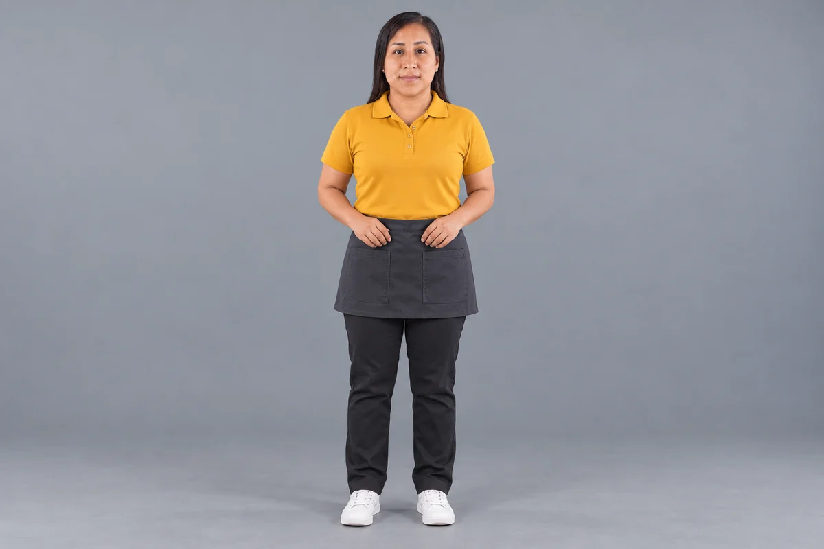 Mujer con polo mostaza y delantal corto grafito con dos bolsillos, vista frontal.