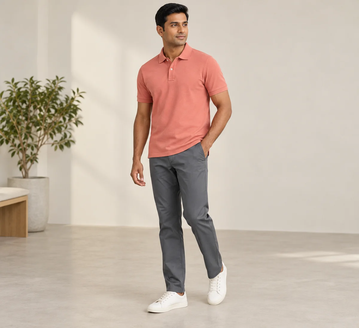 Hombre con polo coral y pantalón gris acero en un interior de muestra.