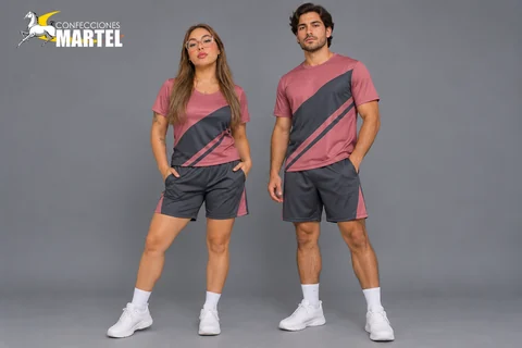 Mujer y hombre con camisetas rosa palo de bloques diagonales grafito y shorts coordinados.